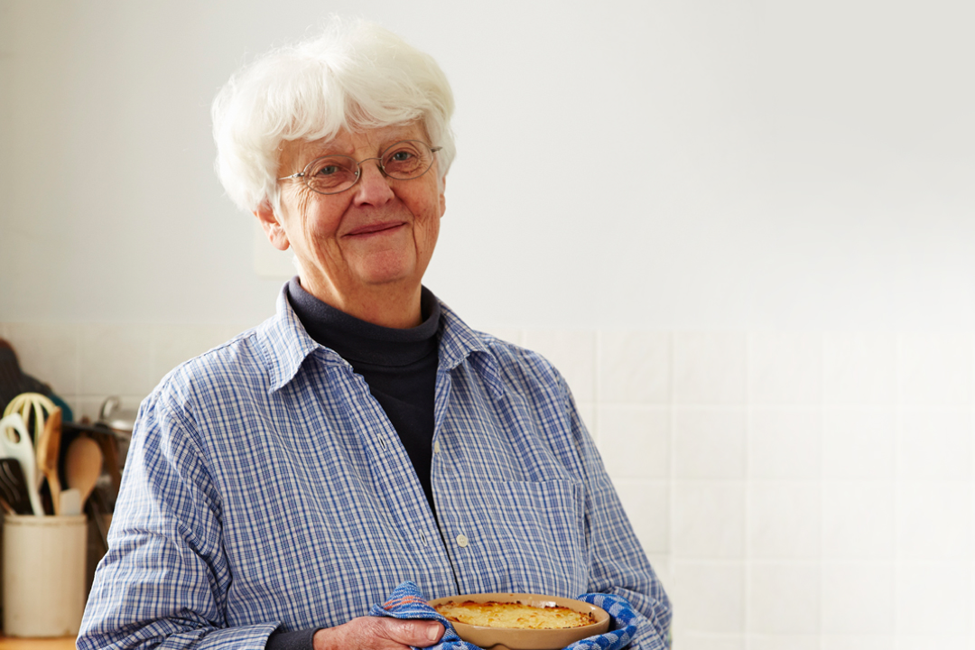 An woman holding a casserole and smiling